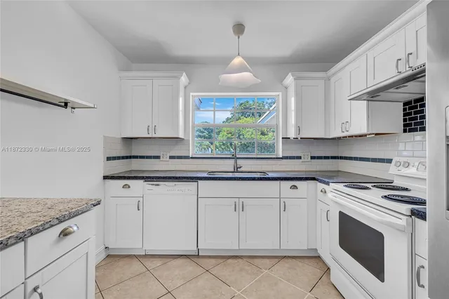 a kitchen with granite countertop white cabinets white stainless steel appliances a sink and a window