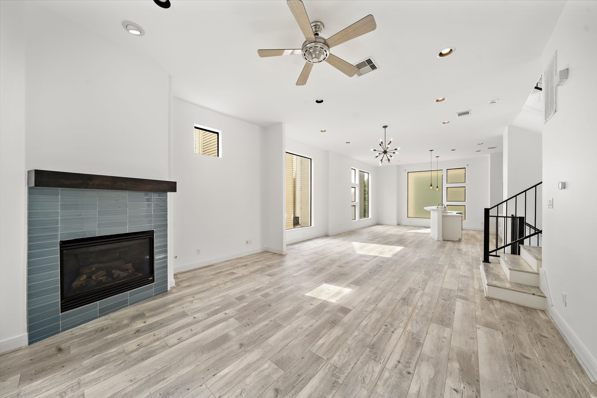 906 Reinerman Street Houston, TX 77007 - Photo 10 of 48 This bright, open-concept living space features modern wood flooring, a cozy fireplace with a sleek tile surround, and stylish pendant lighting. Large windows provide ample natural light, and there's a small staircase leading to another area of the home.