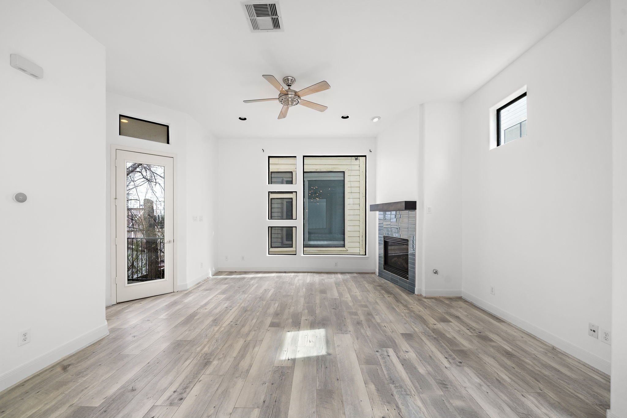 906 Reinerman Street Houston, TX 77007 - Photo 11 of 48 This bright, modern living area features light wood flooring, a ceiling fan, and a sleek corner fireplace. Large windows and a glass door offer plenty of natural light, creating a welcoming and open atmosphere.