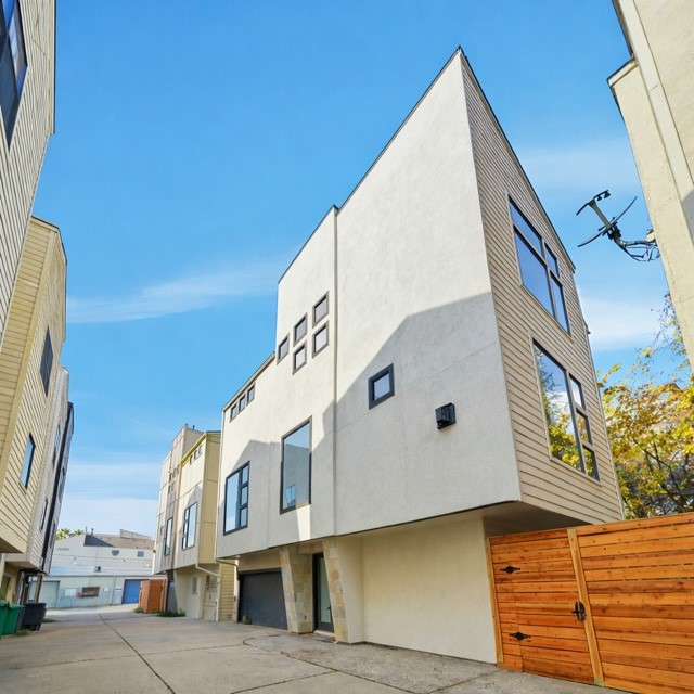 906 Reinerman Street Houston, TX 77007 - Photo 2 of 48 Modern multi-story townhouse with a sleek design, featuring large windows and a wooden privacy fence. The exterior is a mix of light-colored stucco and horizontal siding. Located in a compact urban setting with a shared driveway.