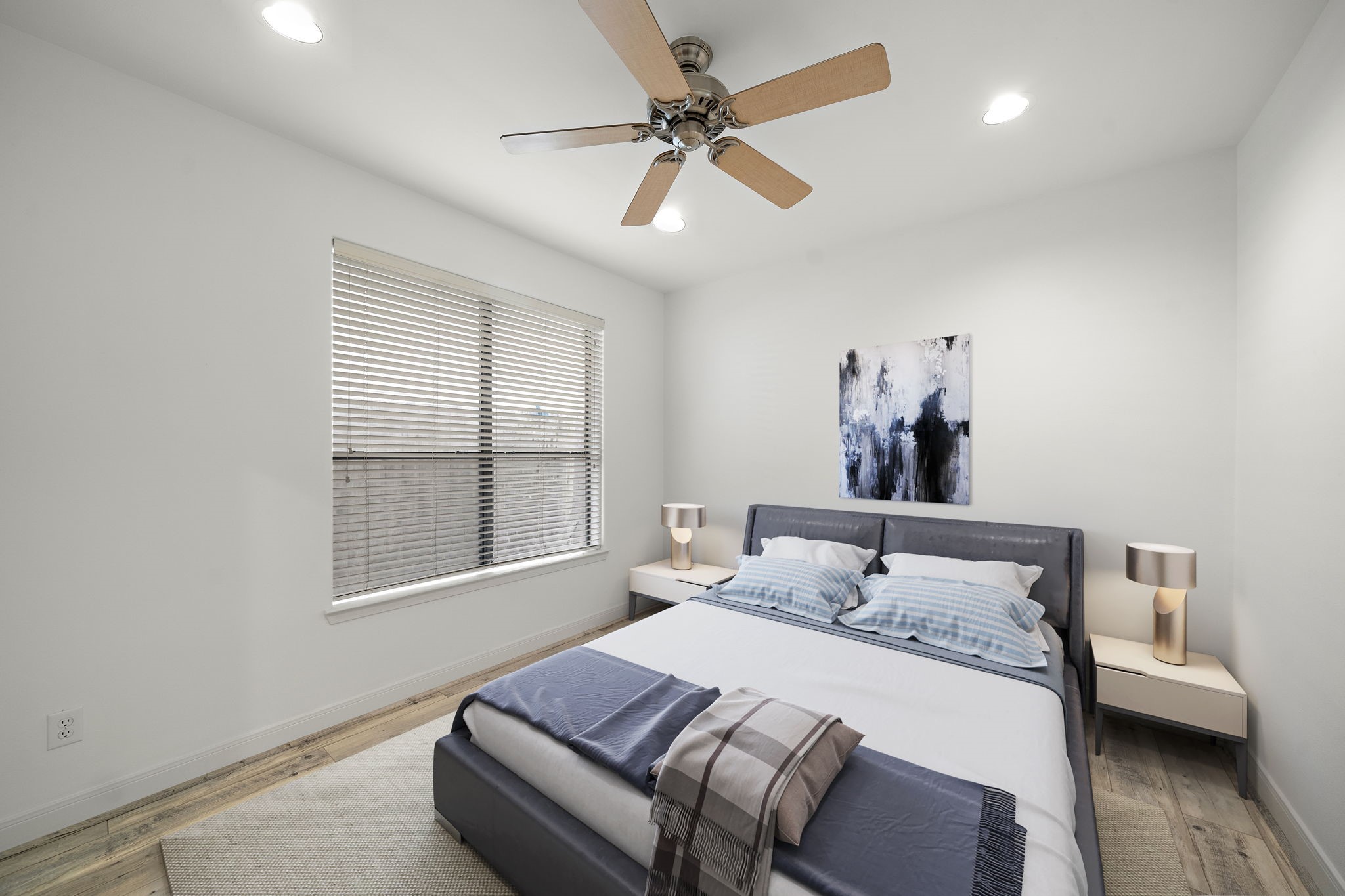 906 Reinerman Street Houston, TX 77007 - Photo 26 of 48 This photo shows a bright, modern bedroom with a large window, wooden floors, and a ceiling fan. The room furnished with a comfortable bed, nightstands (virtual staging) and soft lighting, creating a cozy atmosphere.