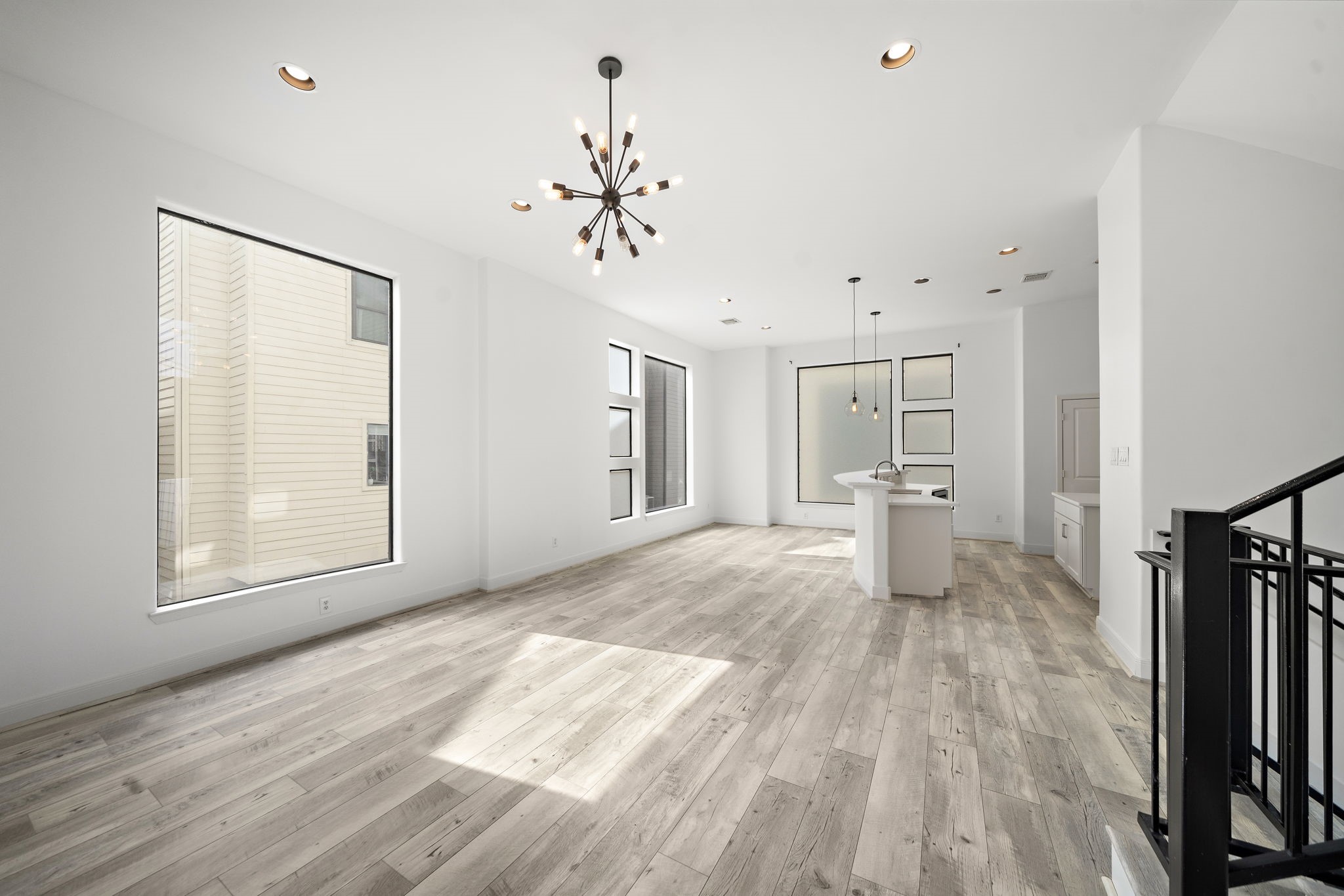 906 Reinerman Street Houston, TX 77007 - Photo 29 of 48 Bright, open-concept living area with large windows, high ceilings, and modern light fixtures. The space features sleek wood flooring and a central kitchen island, perfect for entertaining.