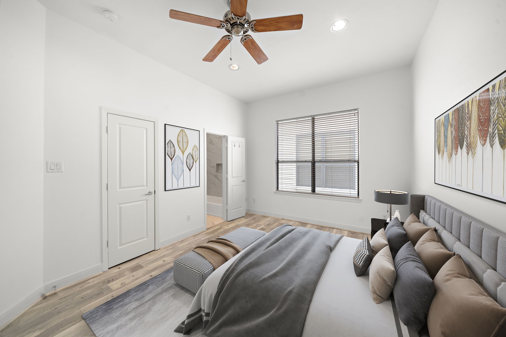 906 Reinerman Street Houston, TX 77007 - Photo 31 of 48 Guest bedroom features a modern design with clean white walls, hardwood floors, and a ceiling fan. It includes a large window with blinds for natural light, a comfortable bed with neutral bedding, and wall art for decoration (Virtual staging furniture) . A door leads to an adjoining bathroom.