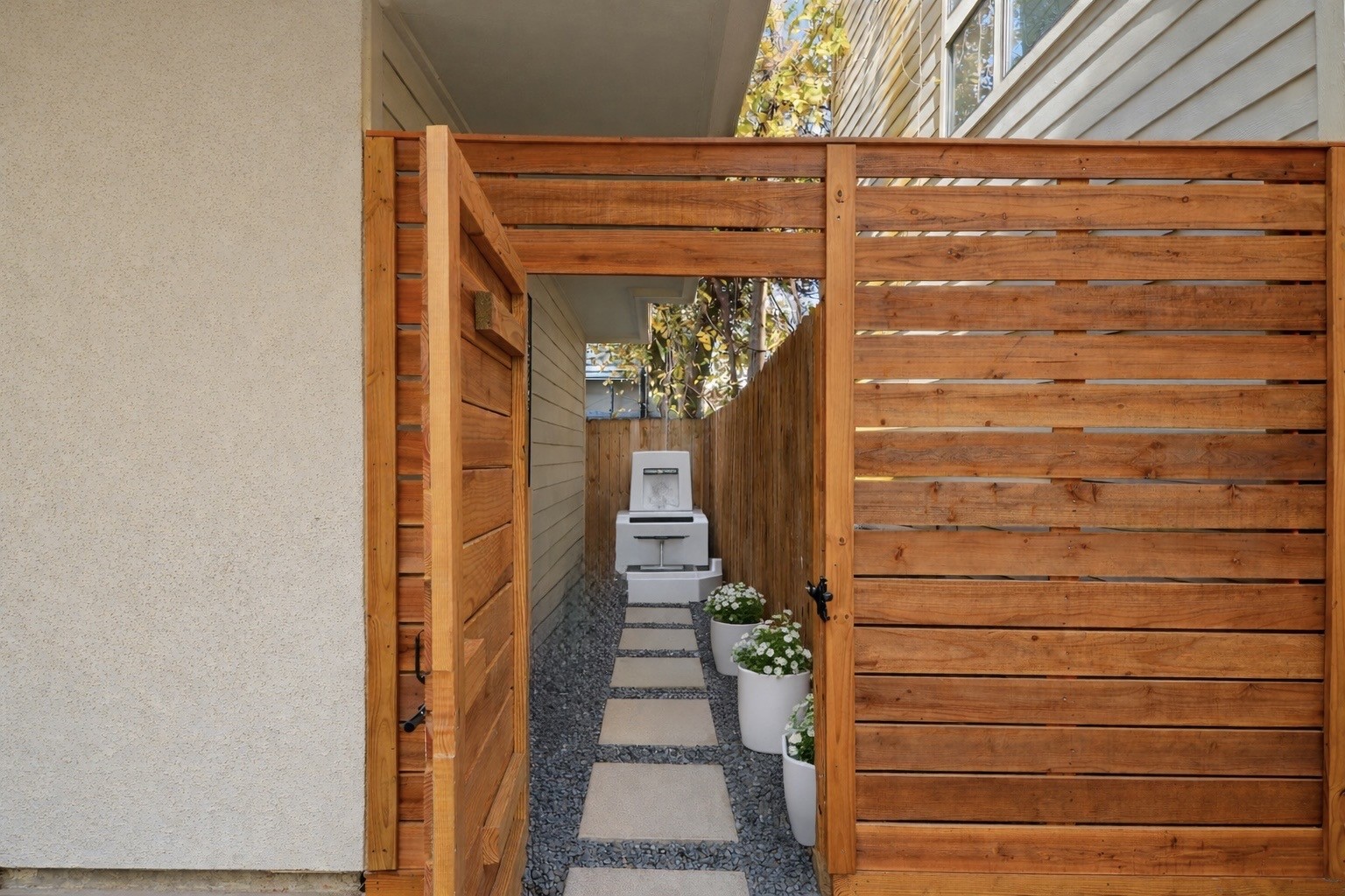 906 Reinerman Street Houston, TX 77007 - Photo 4 of 48 This photo showcases a modern, narrow side yard featuring a wooden privacy fence and gate. The pathway is lined with stepping stones and gravel, leading to a grill area with decorative plants.