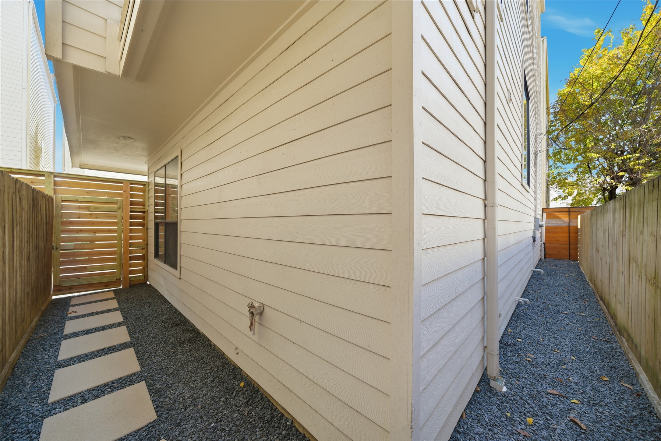 906 Reinerman Street Houston, TX 77007 - Photo 46 of 48 This photo shows a narrow side yard with light-colored siding, gravel ground, and a modern wooden gate. It provides a private, low-maintenance outdoor space.