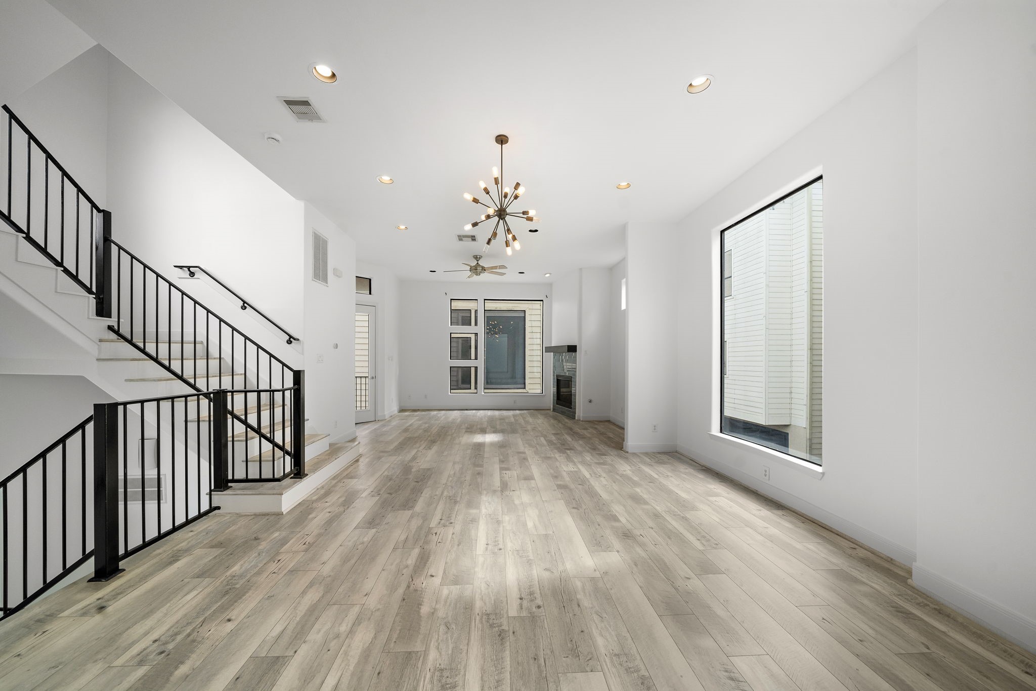 906 Reinerman Street Houston, TX 77007 - Photo 8 of 48 Bright, modern living space featuring light wood flooring, a striking chandelier, large windows, and a sleek staircase with black railings. Ideal for open-concept living.