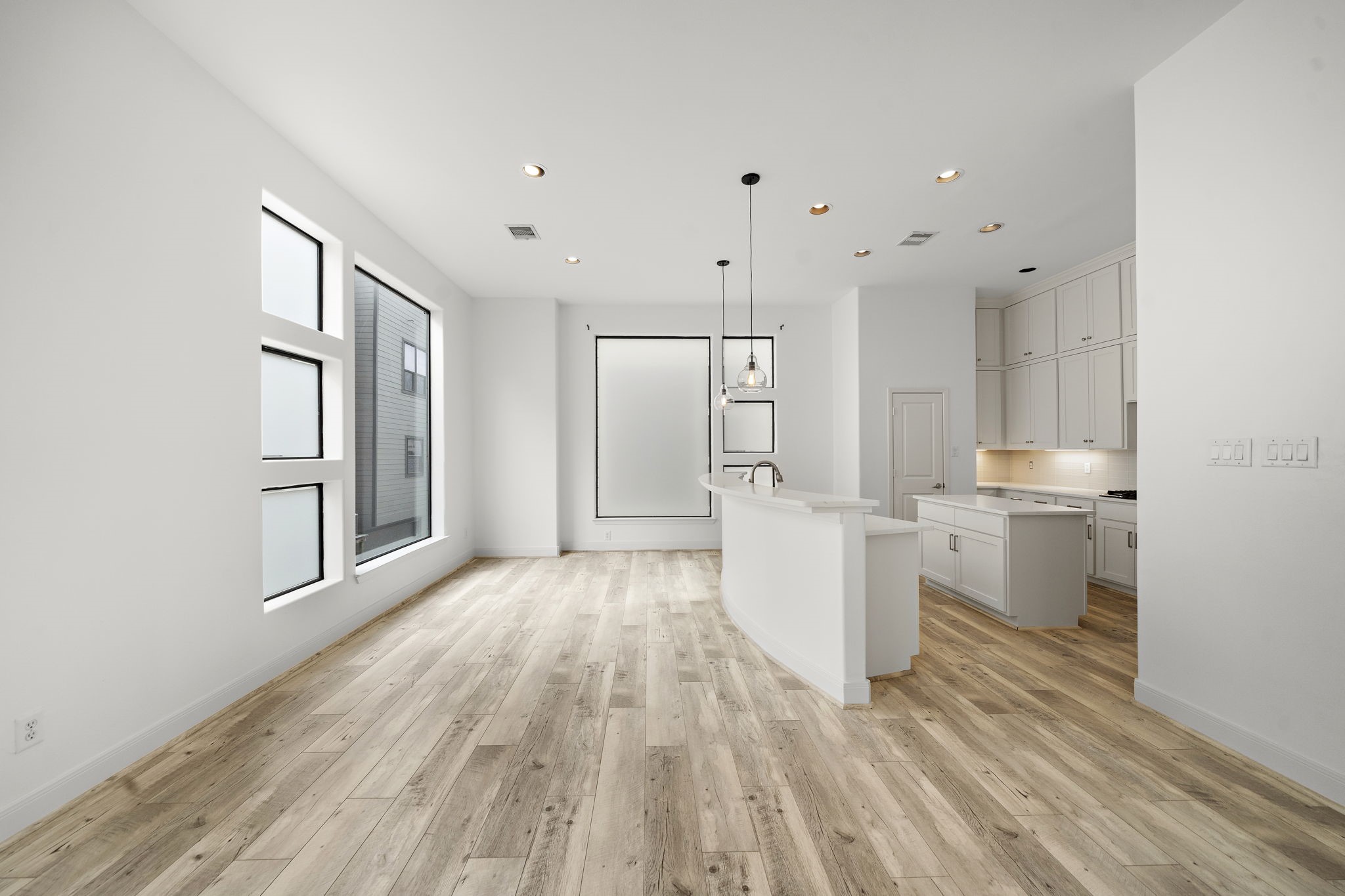 906 Reinerman Street Houston, TX 77007 - Photo 9 of 48 This photo showcases a bright, open-concept kitchen and dining area with modern fixtures, light wood flooring, and large windows that invite natural light. The kitchen features white cabinetry and a sleek island, creating a clean and inviting space.