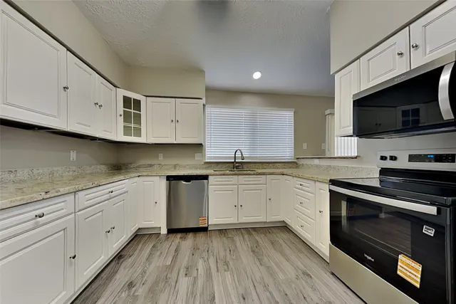 a kitchen with granite countertop a sink dishwasher stove and white cabinets with wooden floor