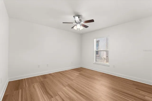 an empty room with wooden floor fan and windows