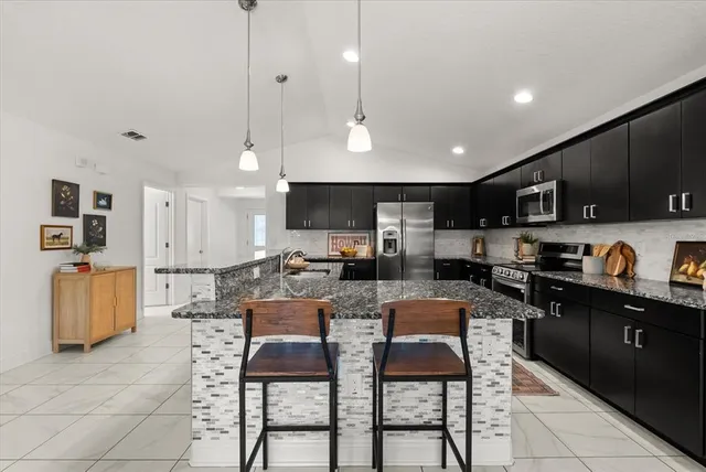 a view of kitchen with stainless steel appliances granite countertop dining table chairs sink and cabinets