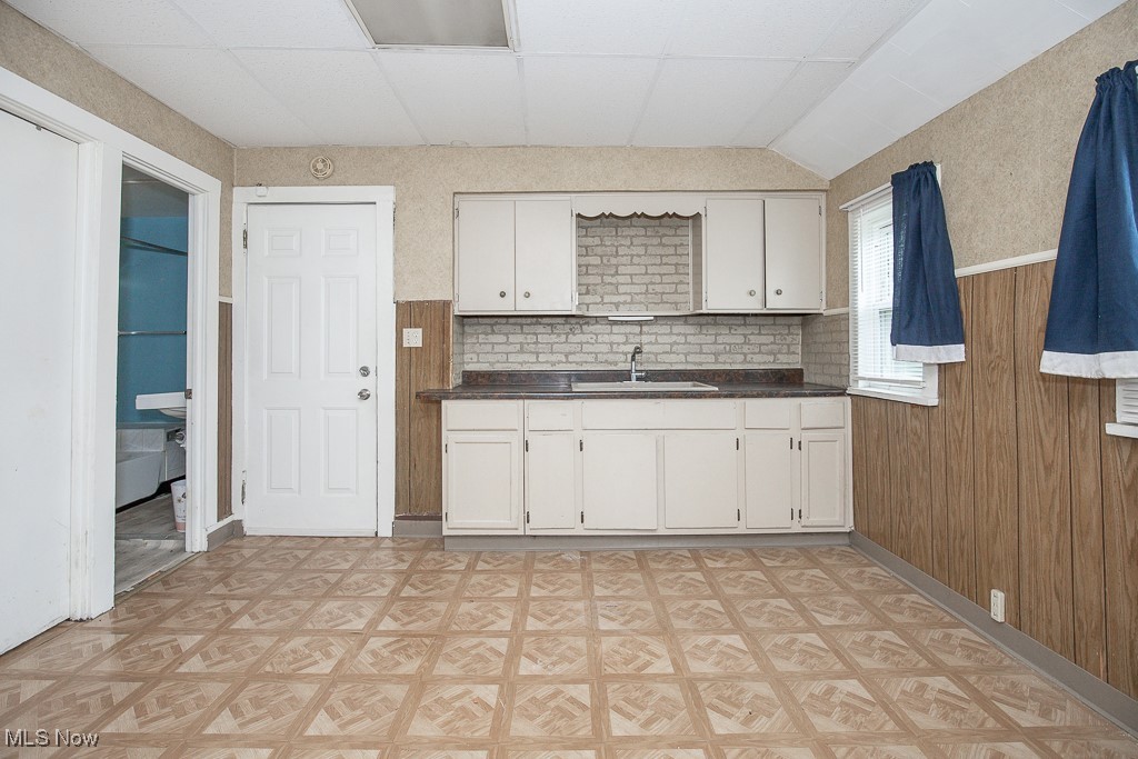 5008 Dolloff Road Cleveland, OH 44127 - Photo 7 of 16 Kitchen featuring a sink, dark countertops, white cabinetry, light flooring, and wood walls