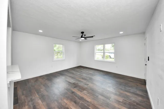 an empty room with wooden floor ceiling fan and windows