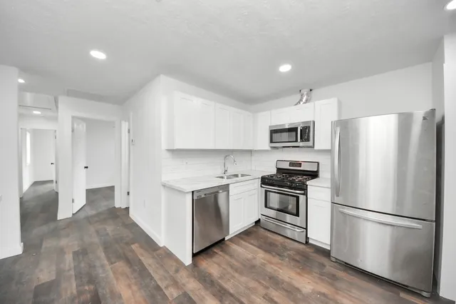 a kitchen with stainless steel appliances a refrigerator a stove top oven a sink and white cabinets