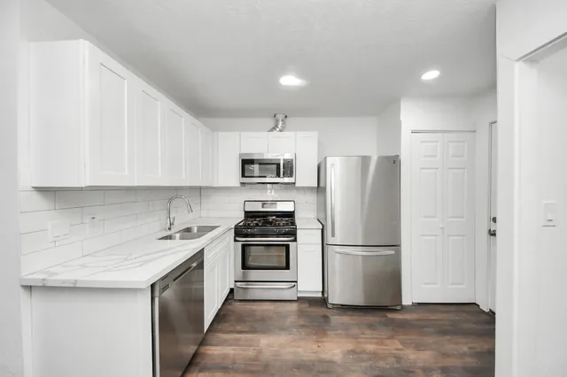a kitchen with a sink a refrigerator and a stove top oven with white cabinets
