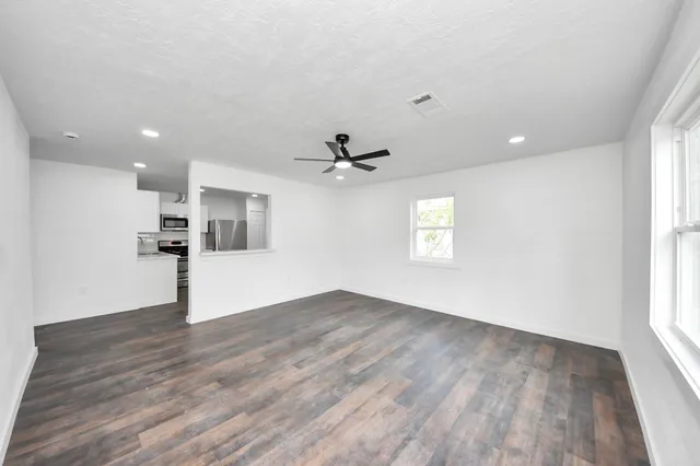 an empty room with wooden floor a ceiling fan white walls and windows