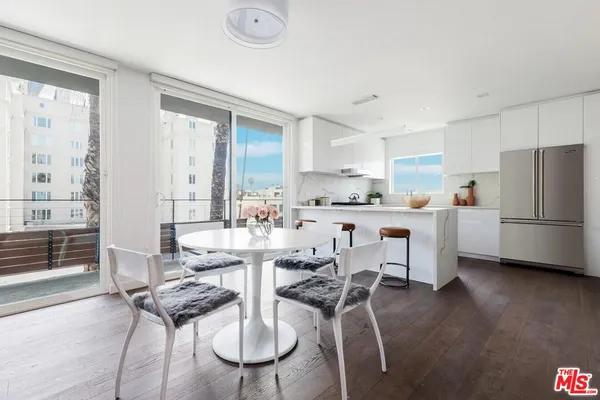 a kitchen with stainless steel appliances kitchen island granite countertop a dining table chairs and a refrigerator