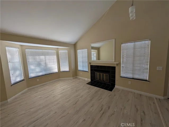 a view of an empty room with wooden floor fireplace and a window