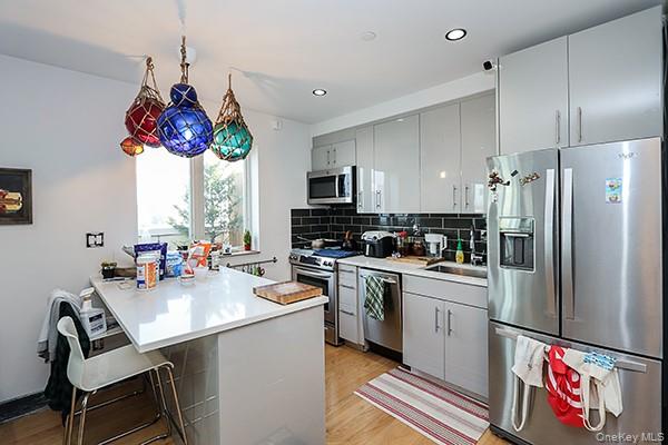 63-34 Fresh Pond Road, Unit 5C Queens, NY 11385 - Photo 9 of 29 Kitchen with appliances with stainless steel finishes, light countertops, a breakfast bar area, light wood-style floors, and decorative backsplash