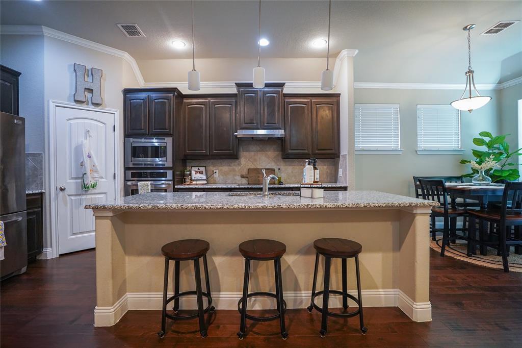 3009 Treasure View Drive Decatur, TX 76234 - Photo 7 of 26 Kitchen with crown molding, decorative backsplash, dark brown cabinetry, a breakfast bar, and decorative light fixtures