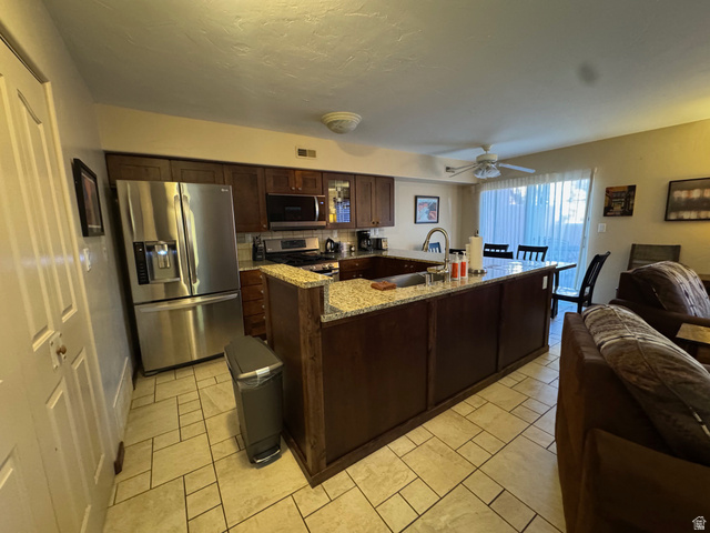 3439 Westwater Road Moab, UT 84532 - Photo 63 of 64 Kitchen with appliances with stainless steel finishes, light stone counters, open floor plan, dark brown cabinets, and ceiling fan