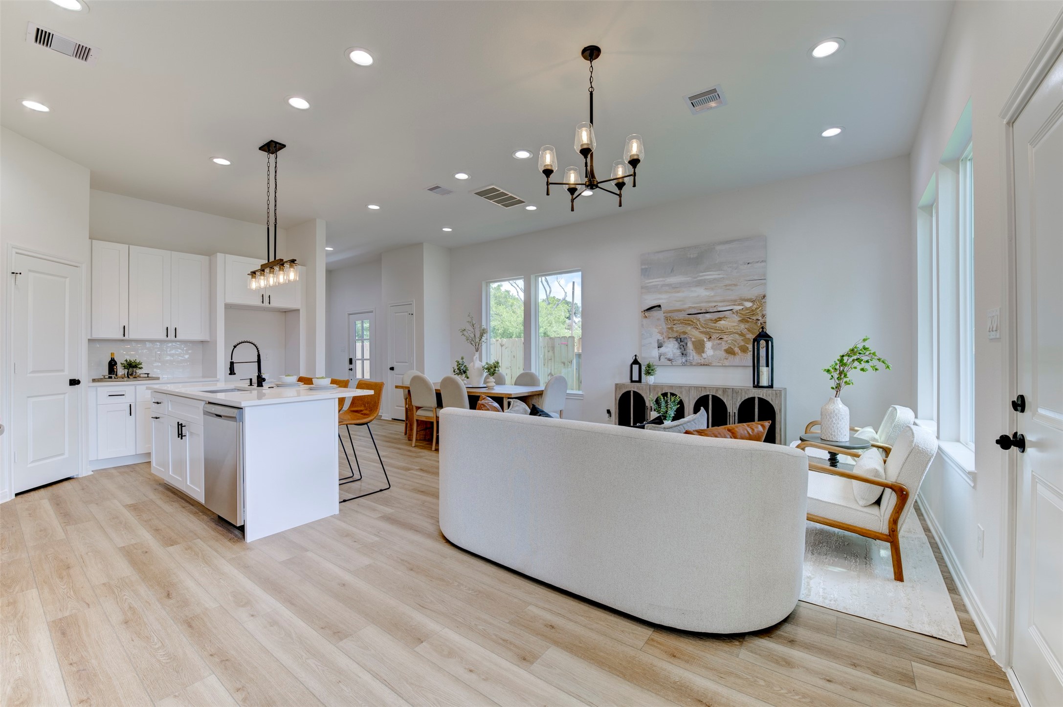 6807 Paris Street Houston, TX 77021 - Photo 13 of 50 Open-concept first floor with hardwood floors, recessed lighting, two pendant chandeliers, white kitchen with island, dining area, and living room all flowing together. Backyard windows bring in natural light.