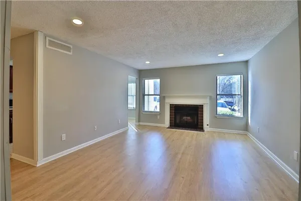 a view of an empty room with wooden floor fireplace and a window