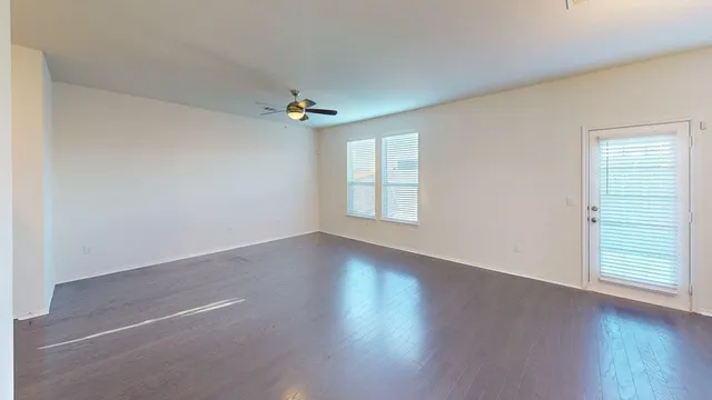 an empty room with wooden floor chandelier fan and windows
