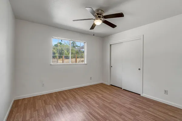 an empty room with wooden floor ceiling fan and windows
