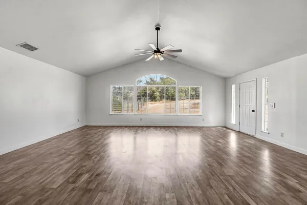 an empty room with wooden floor chandelier and windows