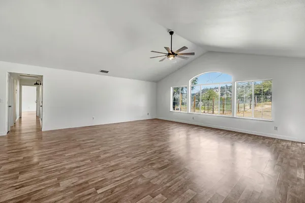 a view of an empty room with wooden floor and fan