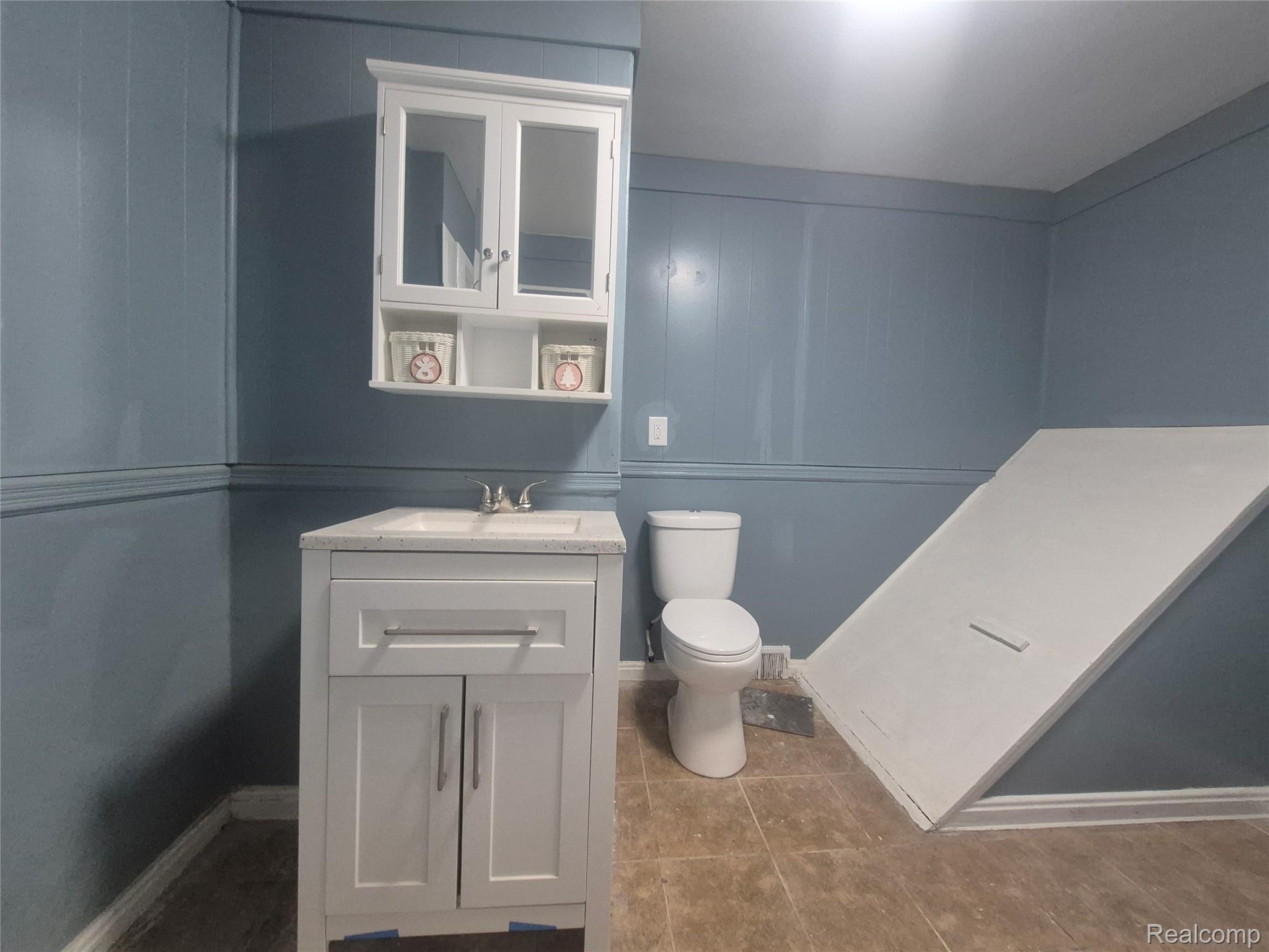 16758 Frazho Road Roseville, MI 48066 - Photo 18 of 53 Pedestal vanity with an integrated sink, wall-mounted medicine cabinet with mirrored doors, paneled walls, and tile flooring