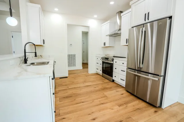a large white kitchen with a sink a refrigerator and wooden floor