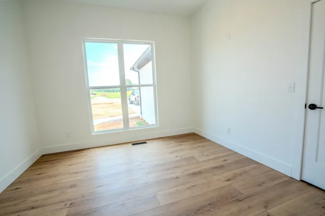 an empty room with wooden floor fan and windows