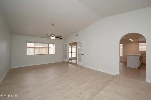 an empty room with chandelier fan and windows