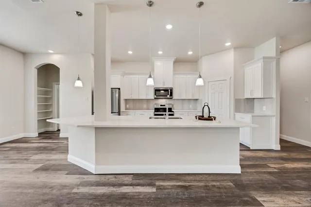 a large white kitchen with kitchen island a sink a center island stainless steel appliances and a cabinets