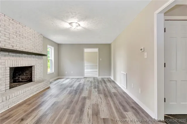 a view of an empty room with wooden floor fireplace and a window