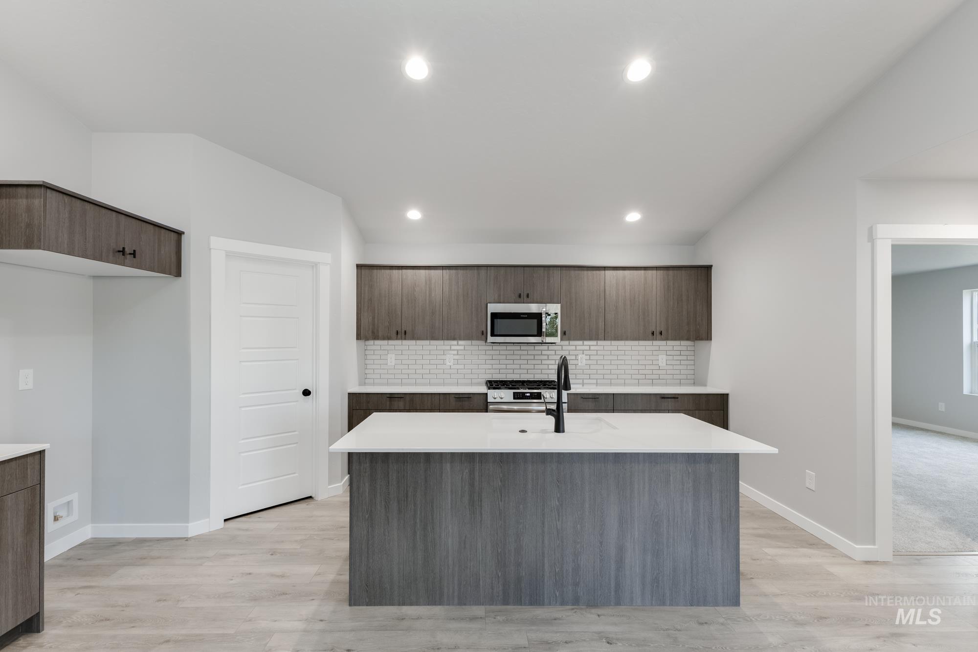 907 North Aleppo Way Meridian, ID 83642 - Photo 3 of 19 Kitchen featuring modern cabinets, a kitchen island with sink, decorative backsplash, dark brown cabinets, and recessed lighting
