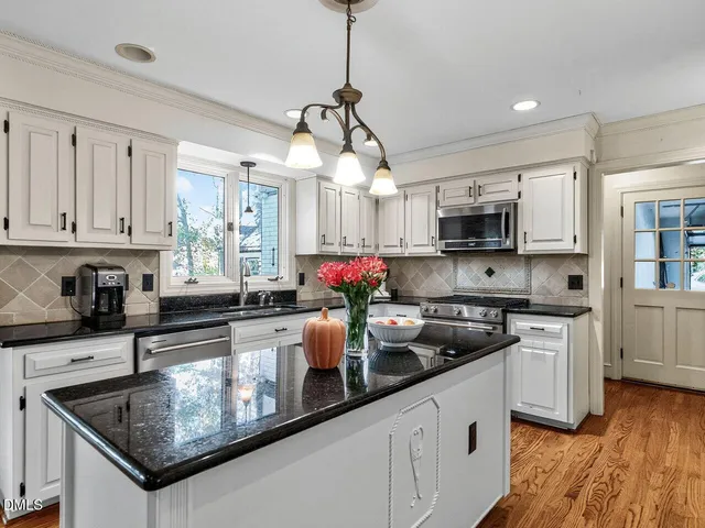 a kitchen with stainless steel appliances granite countertop a sink dishwasher a refrigerator and white cabinets with wooden floor