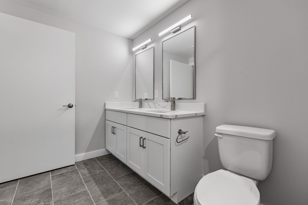 59 Mill Street, Unit 116 Woburn, MA 01801 - Photo 9 of 23 a bathroom with a granite countertop toilet sink and mirror