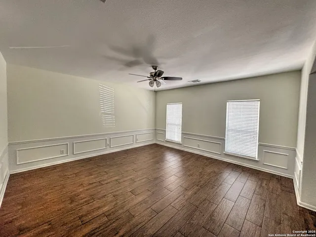 an empty room with wooden floor fan and windows