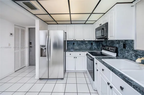 a kitchen with stainless steel appliances granite countertop a refrigerator a sink and white cabinets