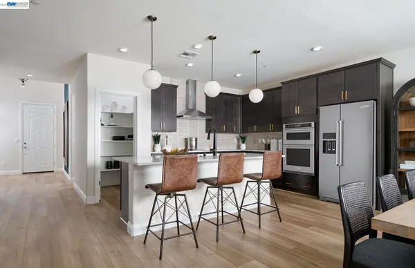 a kitchen with stainless steel appliances kitchen island granite countertop a refrigerator a stove a kitchen island a dining table and chairs with wooden floor