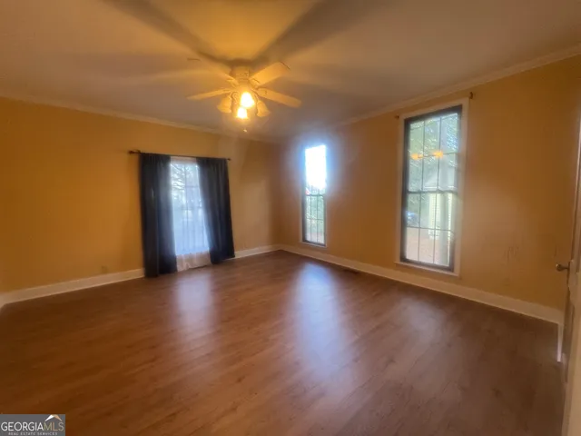 an empty room with wooden floor and windows with curtains
