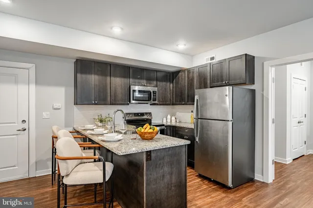 a kitchen with stainless steel appliances a refrigerator a stove a dining table and chairs with wooden floor