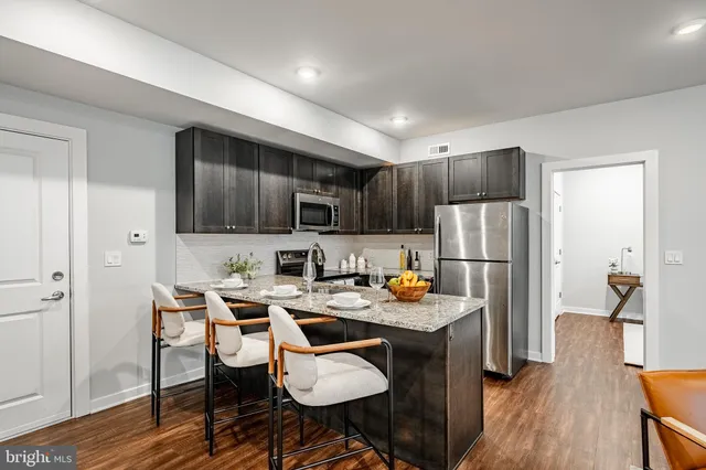 a kitchen with stainless steel appliances granite countertop a refrigerator a stove top oven a sink dishwasher and wooden cabinets with wooden floor