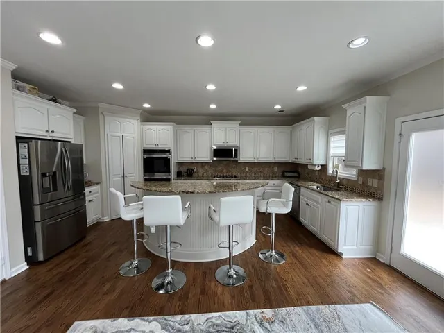 a kitchen with stainless steel appliances kitchen island granite countertop a refrigerator a stove a sink a microwave and white cabinets with wooden floor