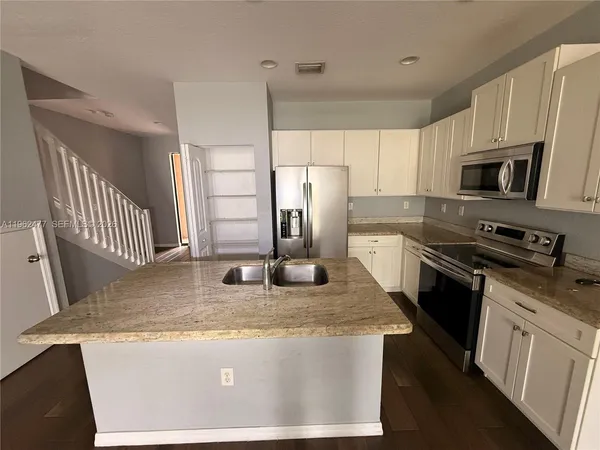 a kitchen with stainless steel appliances a stove a sink a refrigerator white cabinets and wooden floor