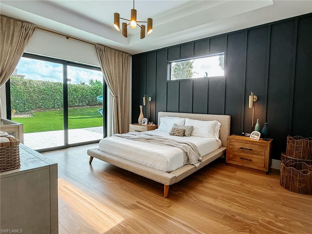 1702 Ludlow Road Marco Island, FL 34145 - Photo 25 of 47 Spacious room featuring wood-finish flooring, a full-height sliding glass door leading to a green lawn, a dark accent wall with horizontal paneling, a horizontal window, and a modern chandelier