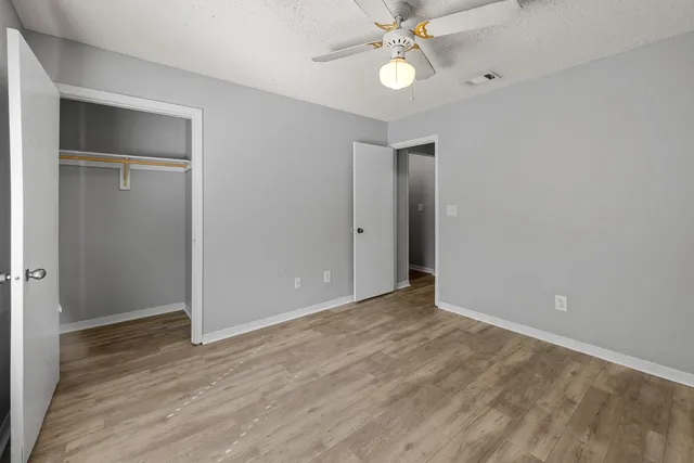 an empty room with wooden floor fan and windows