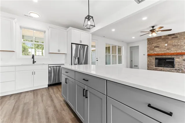 a kitchen with stainless steel appliances a sink dishwasher a stove a refrigerator and white cabinets with wooden floor